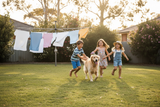 generate an image of kids playing in the backyard with a dog. Ensure there is a washing line in the background